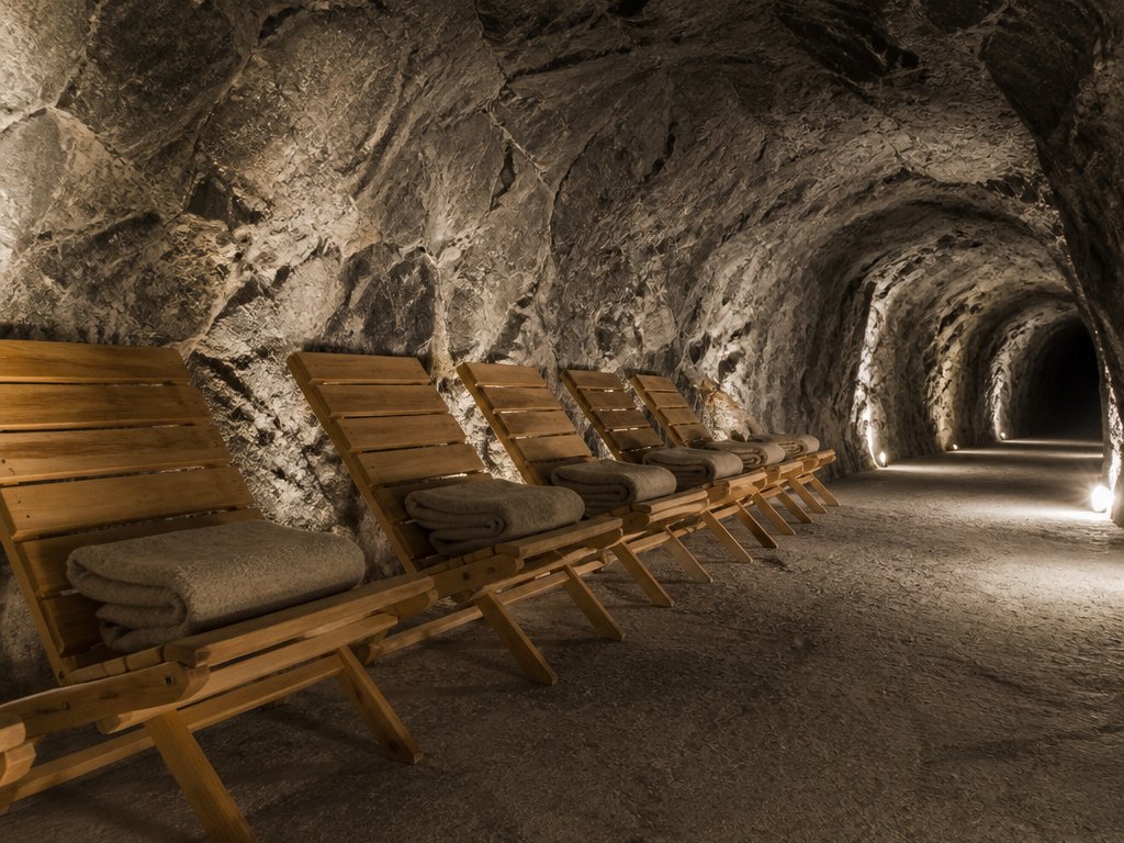 Beleuchteter Stollen mit einer Reihe hölzerner Liegen und gefalteter Decken an der Felswand (mit AI erstelltes Bild)